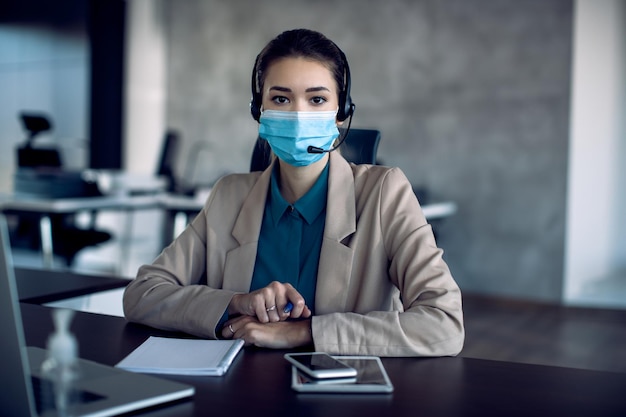 Junge Geschäftsfrau mit schützender Gesichtsmaske bei der Arbeit an ihrem Schreibtisch