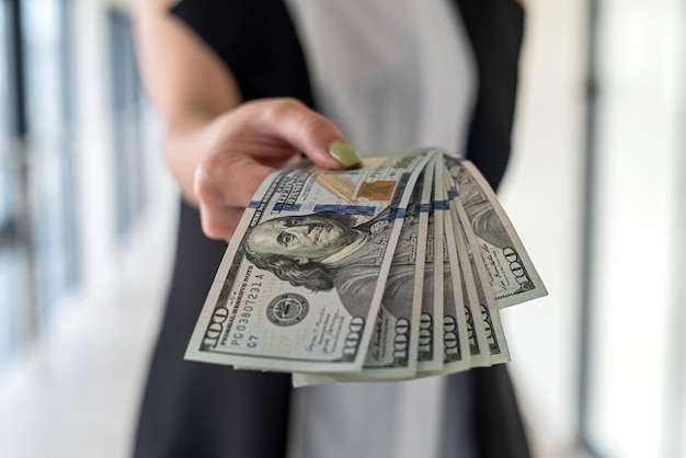 Junge Geschäftsfrau mit US-Dollar-Geld in der Hand steht im Büro. Gehalt ir Bestechungsgeld Konzept