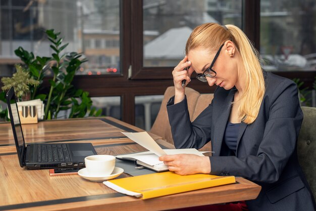 Junge Geschäftsfrau sitzt am Arbeitsplatz und liest Zeitung im Büro