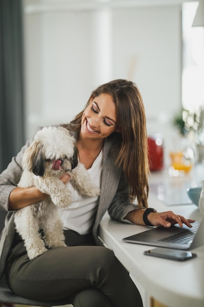 Junge Geschäftsfrau sitzt mit ihrem Hund und benutzt ihren Laptop während der Arbeit von zu Hause aus.