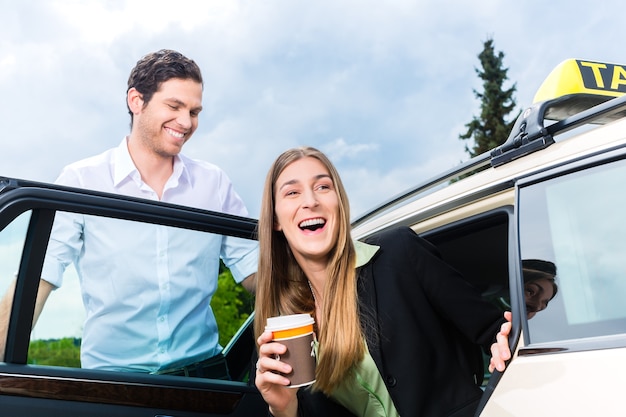 Junge Geschäftsfrau steigt aus dem Taxi, sie hält eine Tasse Kaffee