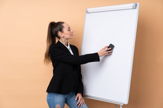 Foto junge geschäftsfrau über isolierter wand, die eine präsentation auf weißer tafel gibt