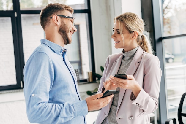 Junge Geschäftskollegen, die Smartphones benutzen und sich im Büro lächeln