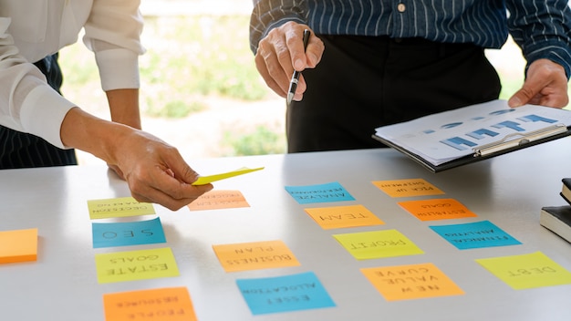 Junge Geschäftsleute, die mit Haftnotizen-Aufklebern posten, erinnern kreatives Brainstorming an Bord des Kollegen in einem modernen Arbeitsraum.