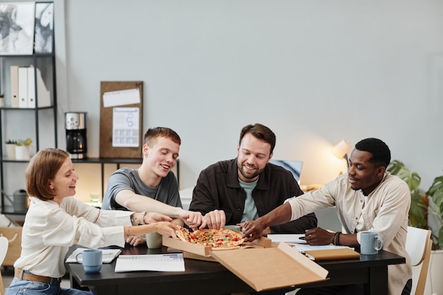 Junge Geschäftsleute, die Pizza zum Mittagessen im Büro bestellen, sitzen am Tisch und genießen ihr Essen