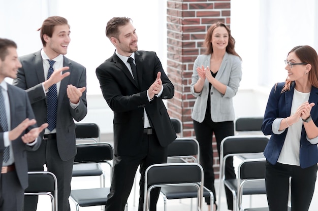Junge Geschäftsleute stehen lächelnd und applaudierend im Büro