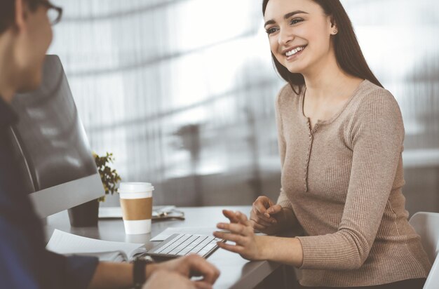 Junge Geschäftsleute unterhalten sich, während sie in einem modernen Büro am Schreibtisch sitzen. Konzentrieren Sie sich auf die Frau. Konzept des Geschäftserfolgs