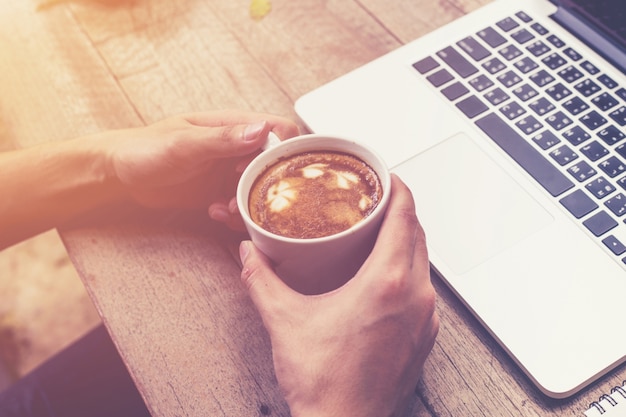 junge Geschäftsmann Hand halten Tasse Kaffee und mit Laptop-Computer in Café mit Vintage getönten.