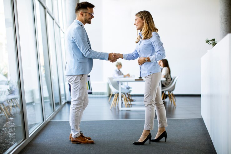 Foto junge geschäftspartner machen handschlag in einem büro, während ihr team im hintergrund arbeitet