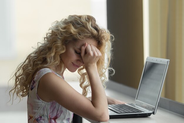 Junge gestresste Frau, die mit Laptop sitzt und den Kopf mit schockiertem Gesichtsausdruck berührt