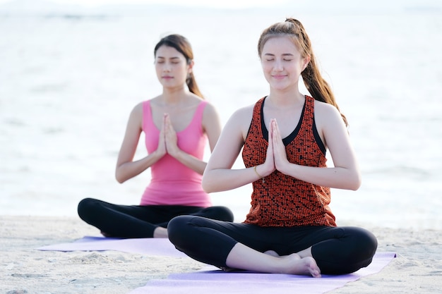 Junge gesunde asiatische Frauen, die Yoga in namaste Haltung auf dem Strand üben