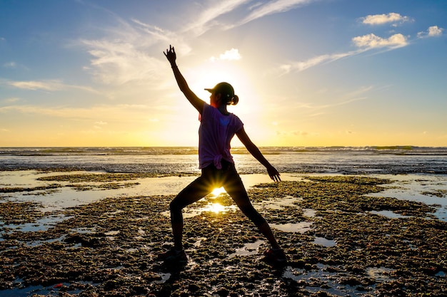 Junge gesunde Frau, die bei Sonnenuntergang Yoga am Strand praktiziert, starkes Selbstvertrauen Frau unter dem Sonnenuntergang