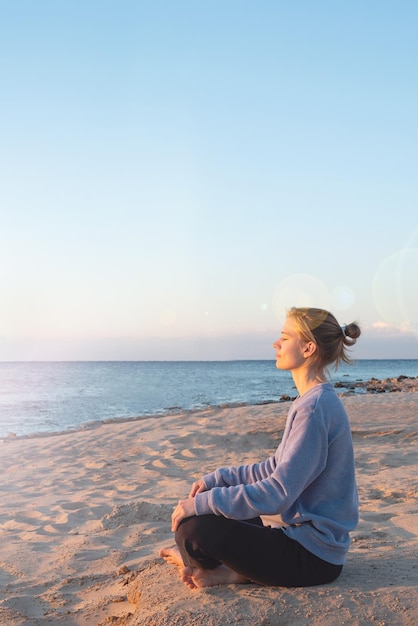 Junge gesunde Frau, die Yoga am Strand bei Sonnenaufgang praktiziert