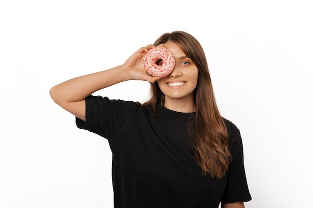 Junge glücklich lächelnde blonde Frau hält einen rosa Donut über ihrem Auge