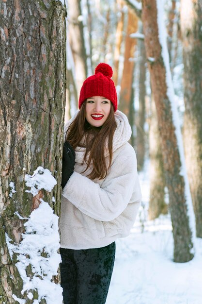 Junge glücklich lächelnde brünette kaukasische Frau steht im schneebedeckten Winterwald Vertikaler Rahmen