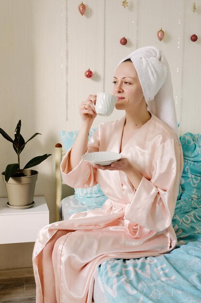 Junge glücklich lächelnde Frau, Braut liegt im Bett im Schlafanzug, Bademantel in einem gemütlichen Zuhause. Wasser trinken.