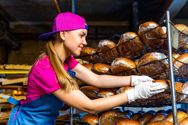 Junge glückliche Arbeiterin in sterilen Tüchern, die frisch gebackene Muffins auf Weißblech in der Lebensmittelproduktionsfabrik halten