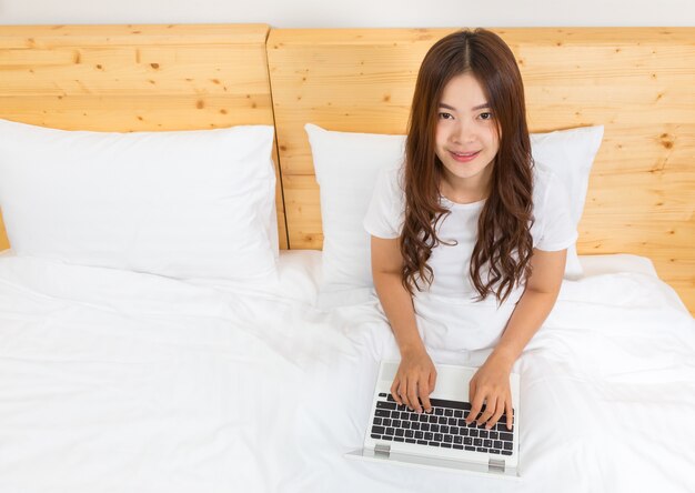 junge glückliche asiatische Frau, die ihren Computer im Bett verwendet