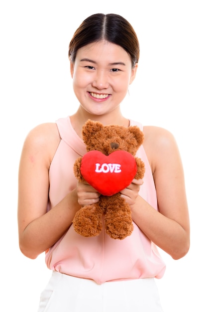 junge glückliche asiatische Frau, die lächelt und Teddybär mit Herz und Liebeszeichen hält