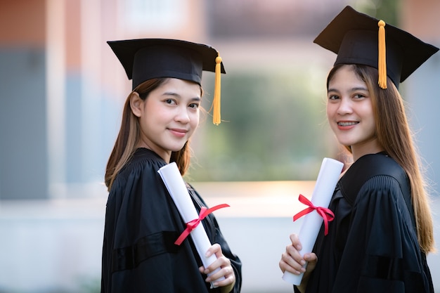 Junge glückliche asiatische Hochschulabsolventen in Abschlusskleid und Mörtel halten ein Abschlusszertifikat und feiern die Bildungsleistung auf dem Universitätscampus. Bildung stockfoto