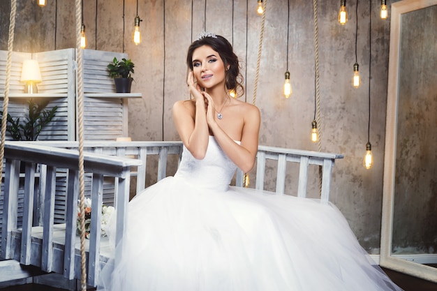 Junge glückliche Braut, die schönes üppiges Kleid im Raum mit vielen Glühbirnen trägt
