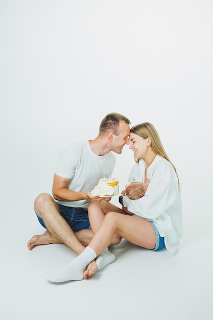 Junge glückliche Eltern mit einem Baby in den Armen und einem Kuchen feiern den ersten Monat des Lebens des Babys Mutter und Vater mit einem Neugeborenen auf weißem Hintergrund