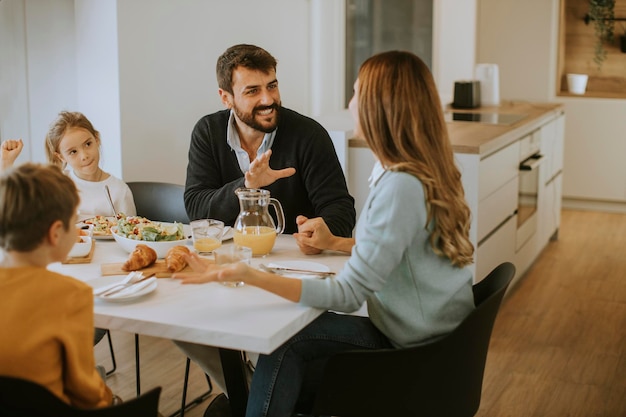 Junge glückliche Familie, die beim Frühstück am Esstisch in der Wohnung spricht