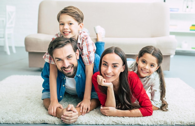 Junge glückliche Familie, die sich zu Hause entspannt, lächelt und sich umarmt, während sie auf dem Boden liegt
