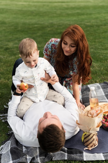 Junge glückliche Familie hat Spaß beim Picknick. Pama Mama und Sohn gehen in der Natur spazieren. Sohn auf der Brust seines Vaters. Familie liegt auf dem Gras im Park. Familienurlaub