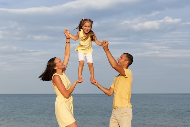 Junge glückliche Familie in gelber Kleidung spielt mit ihrem Kind am Meer