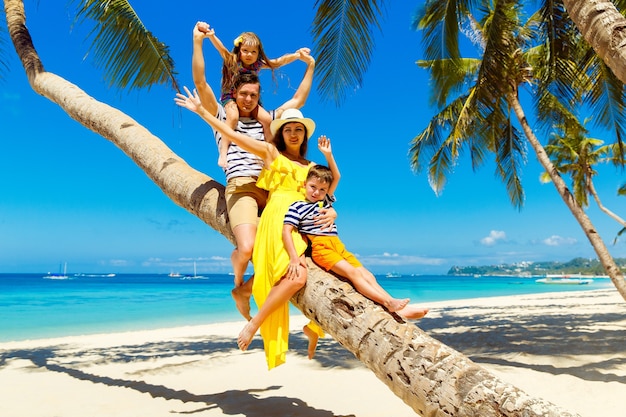 Junge glückliche Familie - Mama, Papa, Tochter und Sohn, die Spaß auf einer Kokospalme an einem tropischen Sandstrand haben. Das Konzept von Reisen und Familienurlaub.