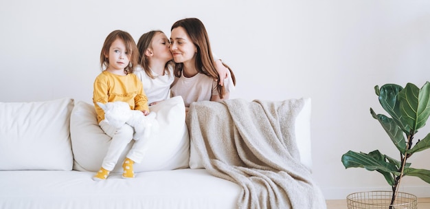 Junge glückliche Familie mit einer Elternteilfrau Mutter mit zwei Kindern Mädchen auf der Couch im Wohnzimmer mit grüner Zimmerpflanze zu Hause