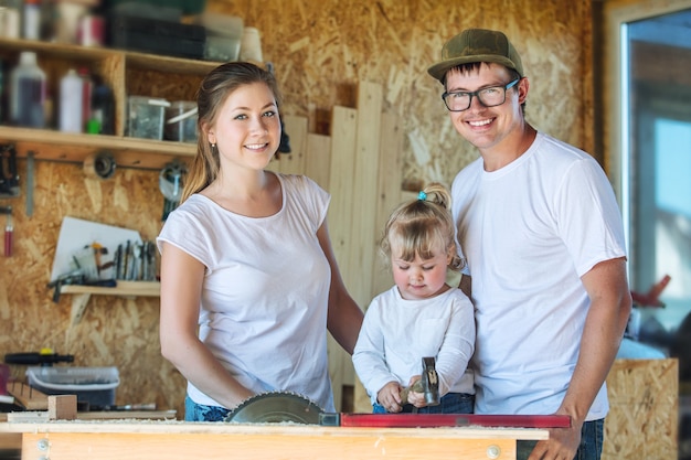 Junge glückliche Familienmutter, -vater und -baby in der Tischlerei, die mit Werkzeugen arbeitet