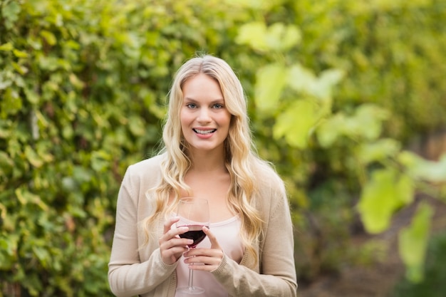 Junge glückliche Frau, die ein Glas Wein hält und Kamera betrachtet
