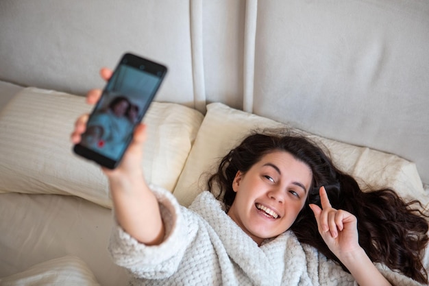 Junge glückliche Frau, die eine Selfie-Geschichte macht, die sich im Bett niederlegt