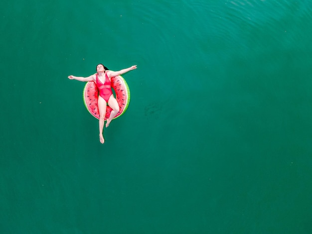 Junge glückliche Frau, die in blauem azurblauem Wasser auf aufblasbaren Ringkreis-Sommerferien schwimmt