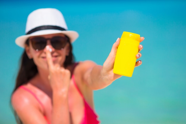 Junge glückliche Frau, die Sonnenschutzmittel auf ihrer Nase auf weißem Strand anwendet