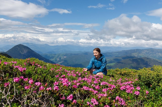 Junge glückliche Frau, die unter blühendem wildem Rhododendron sitzt Rhododendronblumen blühen auf