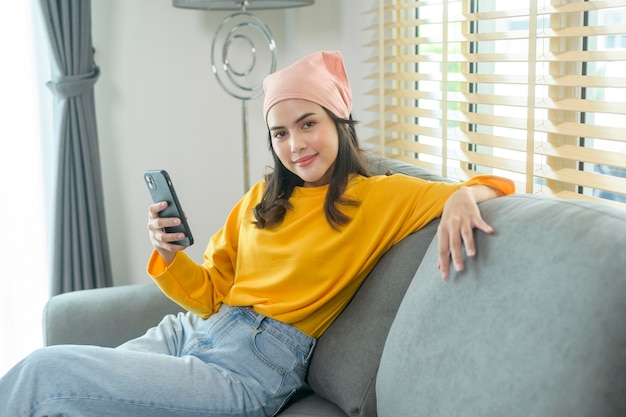 Junge glückliche Frau entspannt sich und benutzt Smartphone im Wohnzimmer