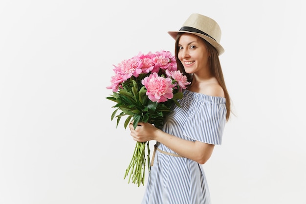 Junge glückliche Frau im blauen Kleid, Hut, der Blumenstrauß der schönen rosa Pfingstrosen hält, die auf weißem Hintergrund lokalisiert werden. Valentinstag, Internationaler Frauentag-Feiertagskonzept. Werbefläche.