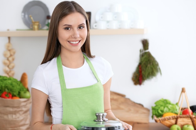 Junge glückliche Frau in einer grünen Schürze, die in der Küche kocht Hausfrau fand ein neues Rezept für ihre Suppe Gesundes Essen und vegetarisches Konzept