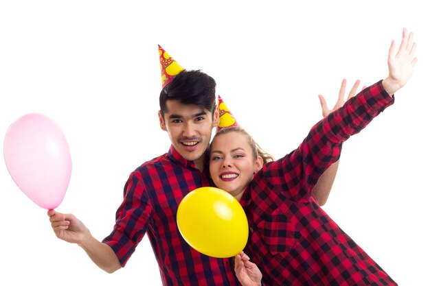 Junge glückliche Frau mit kastanienbraunem Pferdeschwanz und gutaussehender Mann mit feiernden Hüten, die Luftballons blasen