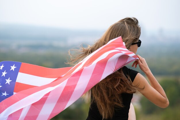 Junge glückliche frau mit langen haaren, die auf der amerikanischen nationalflagge des windes winken