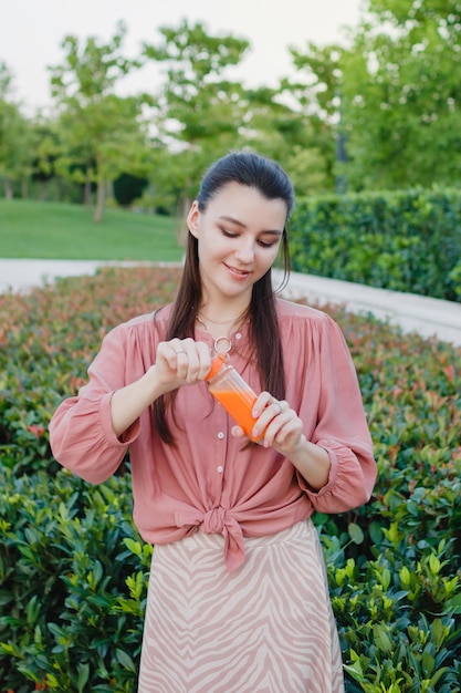 Junge glückliche Frau öffnet eine Flasche mit frisch gepresstem Orangensaft Sommertag im Freien im Park