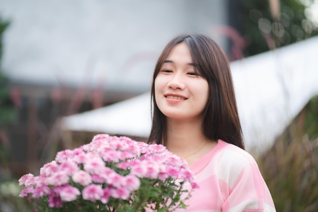 Junge glückliche Frauenperson, die mit der rosa Blume lächelt, die hübsches nettes Mädchenporträt im Sommer mit Naturblumenpflanze in der rosa Farbe und im bunten natürlichen Freien blüht