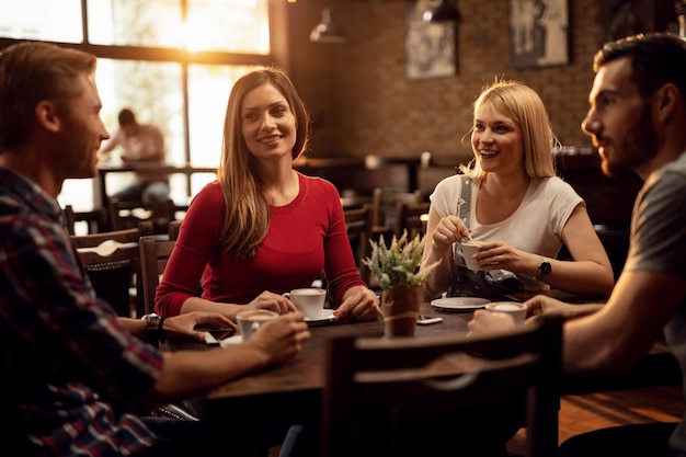 Junge glückliche Freunde, die Kaffee trinken und sich unterhalten, während sie sich in einem Café versammeln. Der Fokus liegt auf Frauen