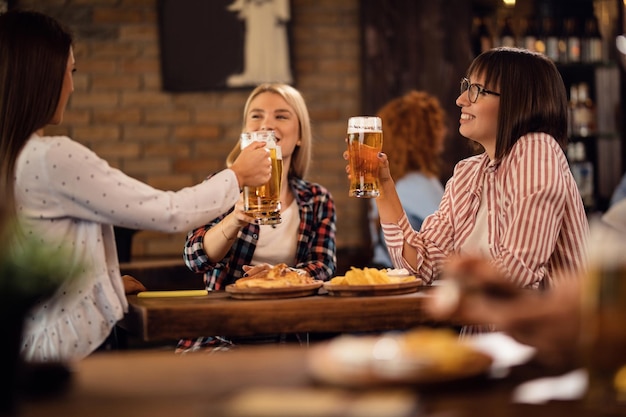 Junge glückliche Freundinnen amüsieren sich beim Toasten mit Bier in einer Kneipe