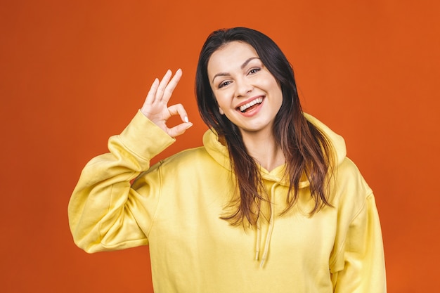 Junge glückliche fröhliche Frau, die ok Zeichen lokalisiert gegen orange Hintergrund zeigt.