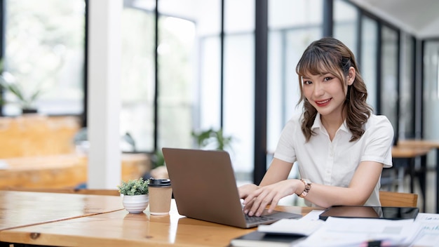 Junge glückliche Geschäftsfrau, die Computer im modernen Büro verwendet