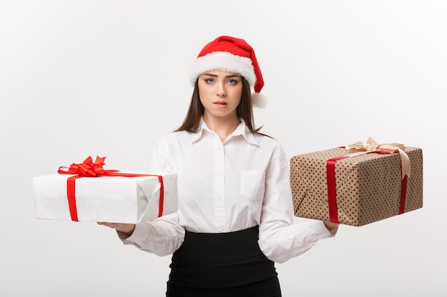 Junge glückliche kaukasische Geschäftsfrau des Weihnachtskonzepts mit Weihnachtsmütze, die Geschenkboxen mit Kopienraum auf der Seite wählt